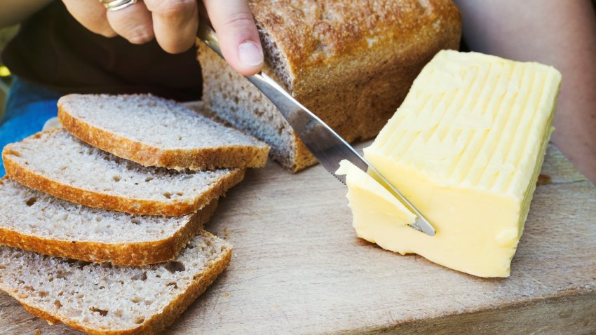 A person with a knife slicing through a block of butter for a sliced bread loaf.