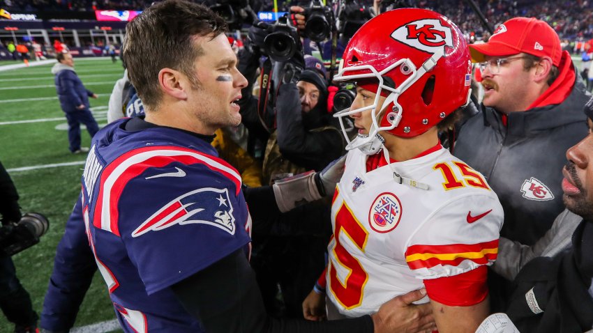 Tom Brady, n a blue Patriots uniform, extends his arm to greet Patrick Mahomes, who is wearing a white Chiefs Jersey and red KC helmet